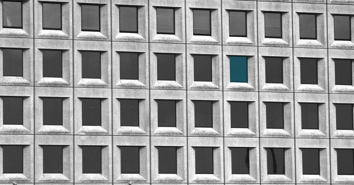 Black and white office building facade with one window highlighted in teal among identical windows